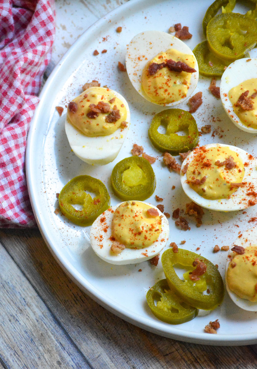 smoked deviled eggs garnished with bacon and smoked paprika on a white plate with pickled jalapenos