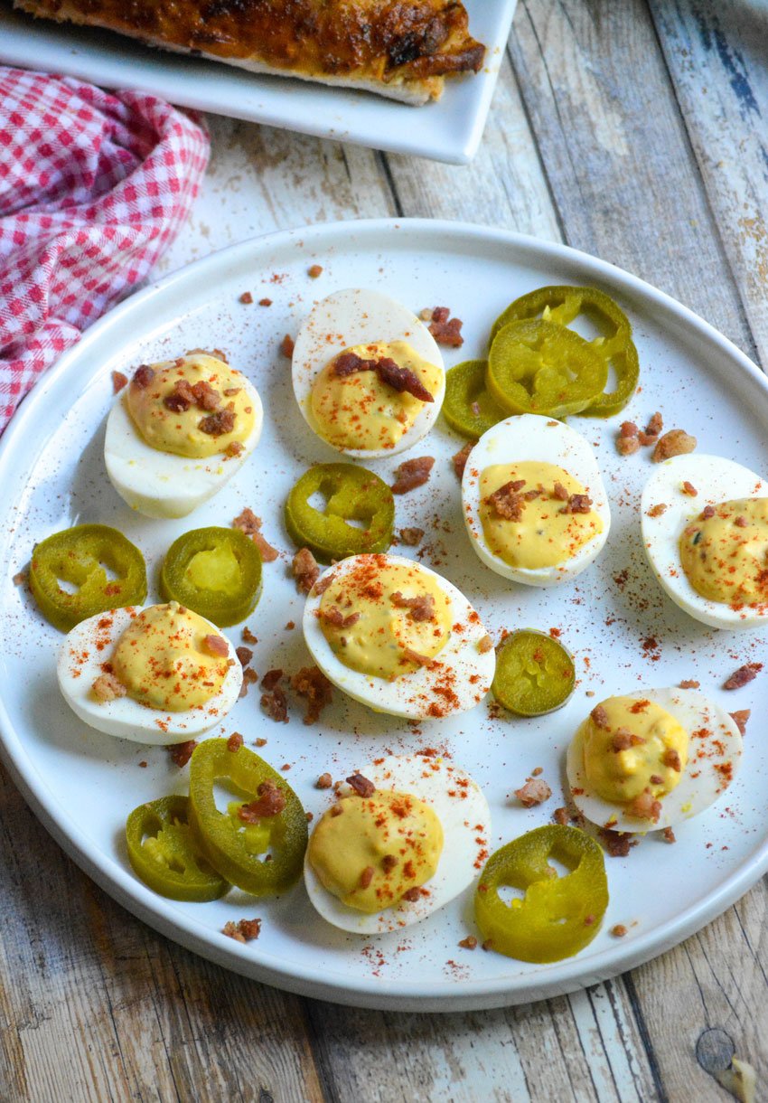 smoked deviled eggs on a white plate with pickled jalapeno slices