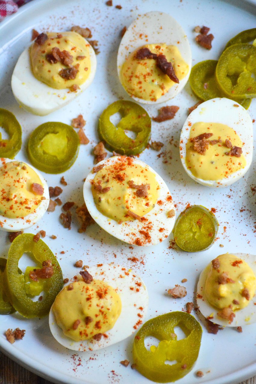 smoked deviled eggs on a white plate with pickled jalapeno slices