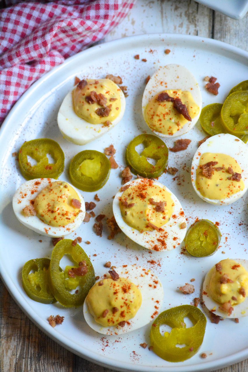smoked deviled eggs garnished with bacon and smoked paprika on a white plate with pickled jalapenos