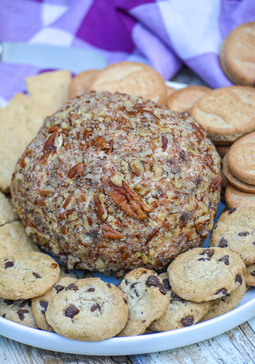 a nut covered dessert cheese ball on a white plate surrounded by cookies