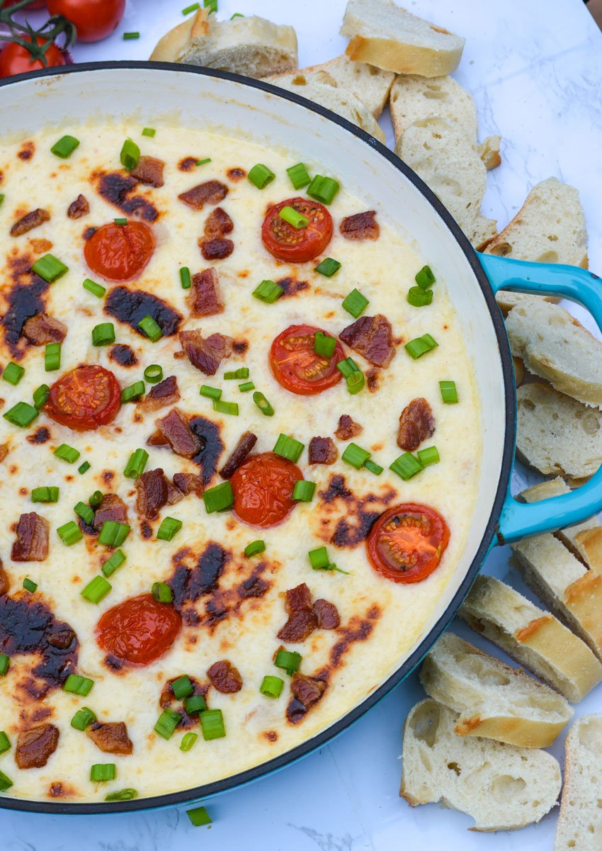kentucky hot brown dip in an enameled cast iron skillet with a fresh baguette slices on the side
