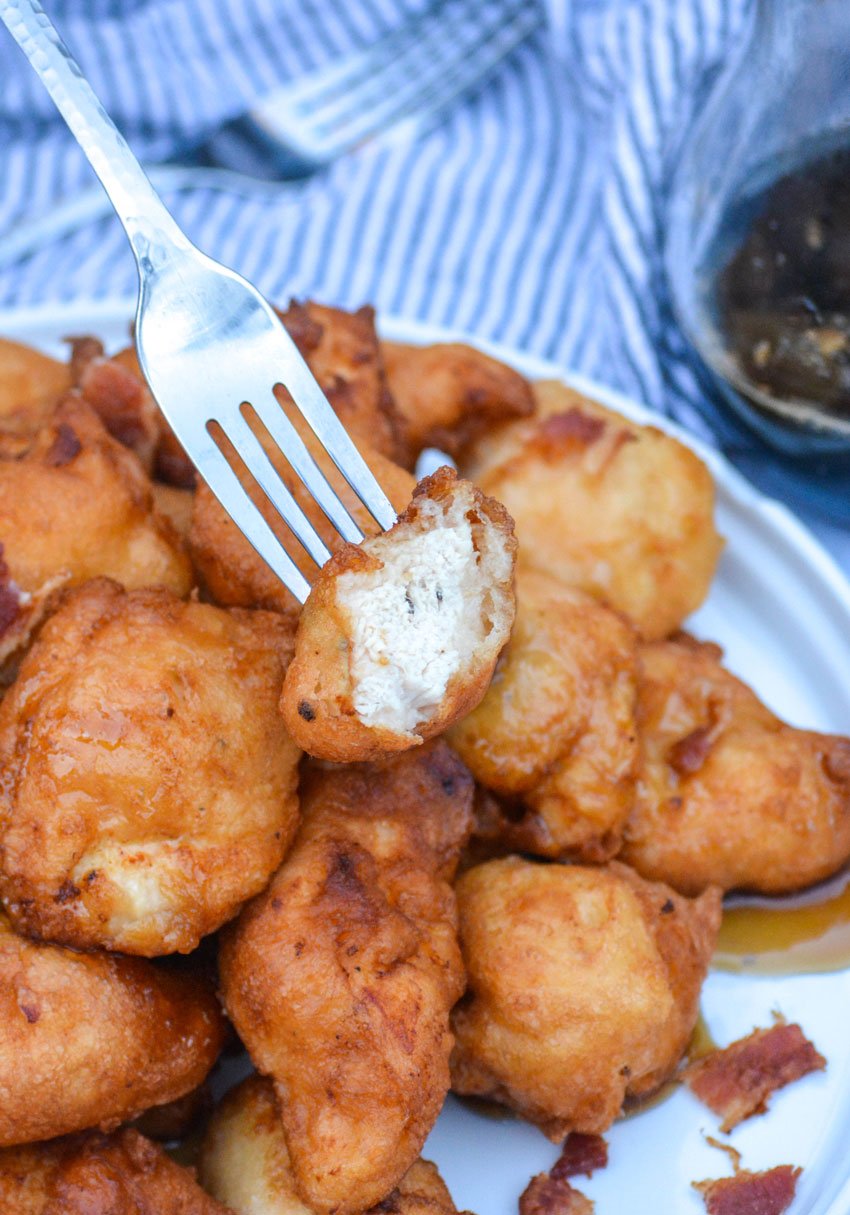 a silver fork holding up a syrup dipped pancake battered chicken nugget