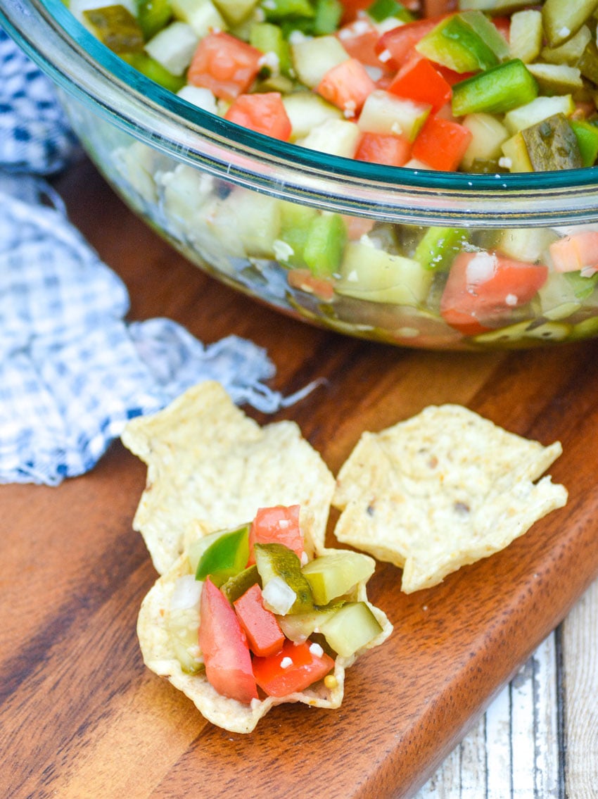 scooped tortilla chips topped with pickle de gallo on a wooden cutting board