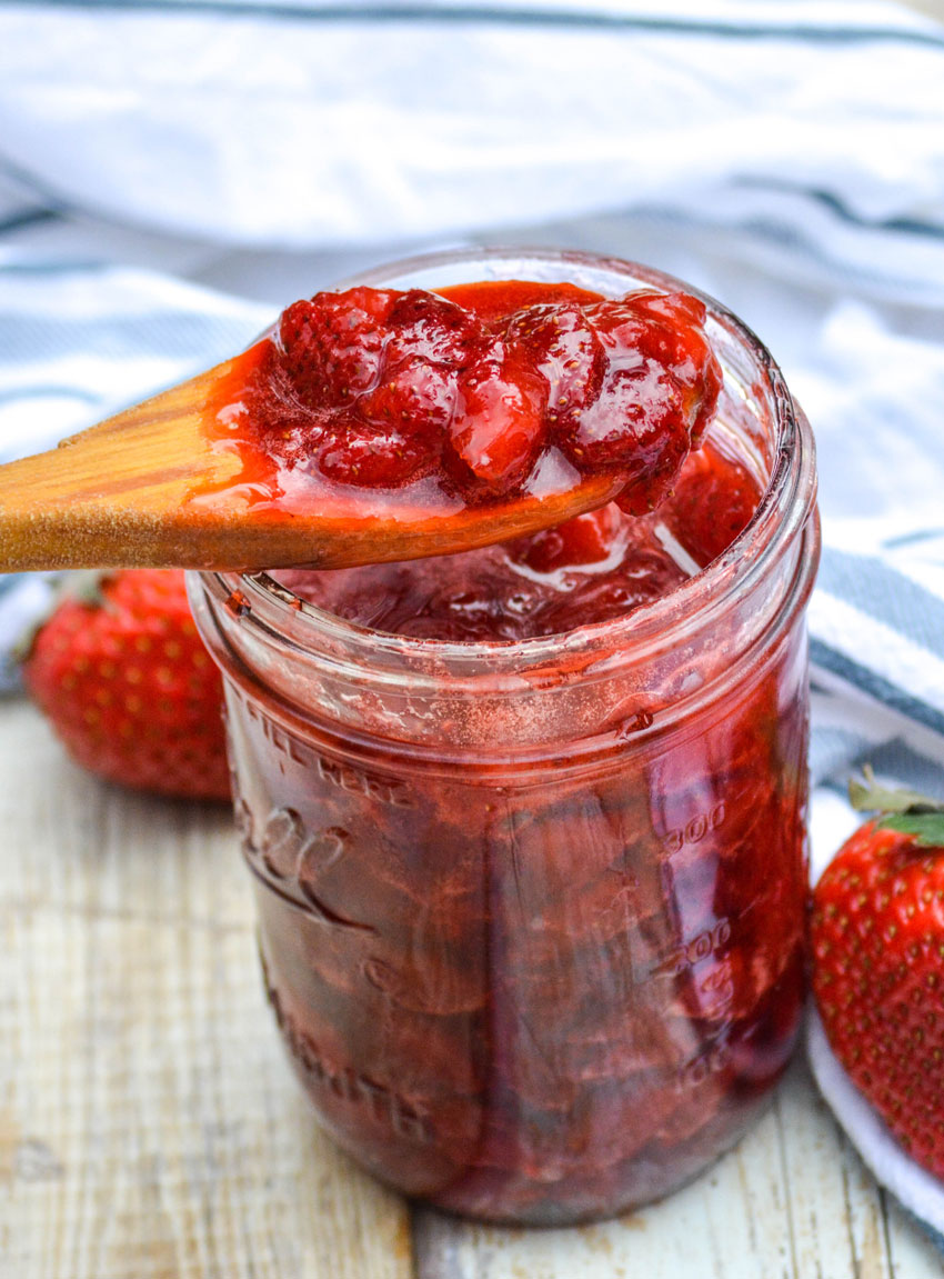 a wooden spoon scooping homemade strawberry sauce out of a glass jar
