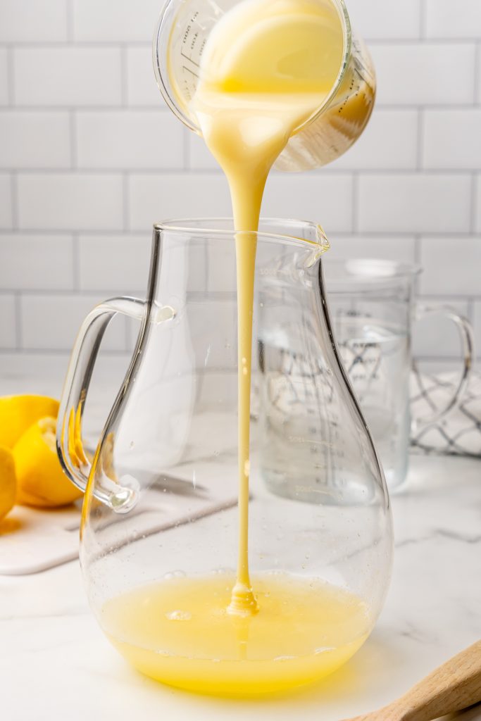 condensed milk being poured into a large glass pitcher