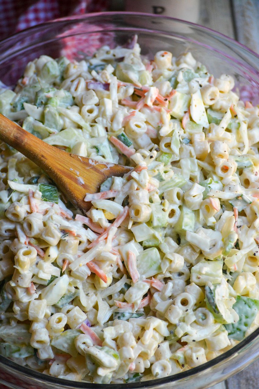 a wooden spoon in a bowl of creamy coleslaw pasta salad