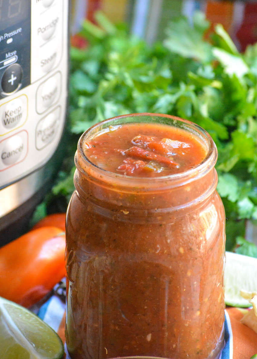 Instant pot salsa in a glass mason jar in front of an instant pot and fresh herbs