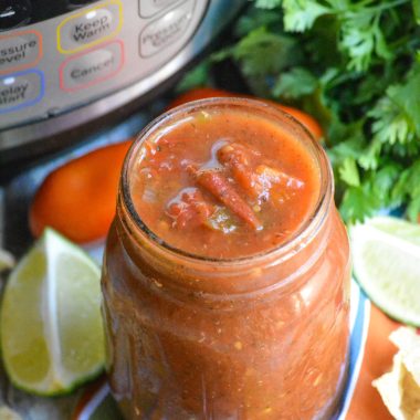 Instant pot salsa in a glass mason jar in front of an instant pot and fresh herbs