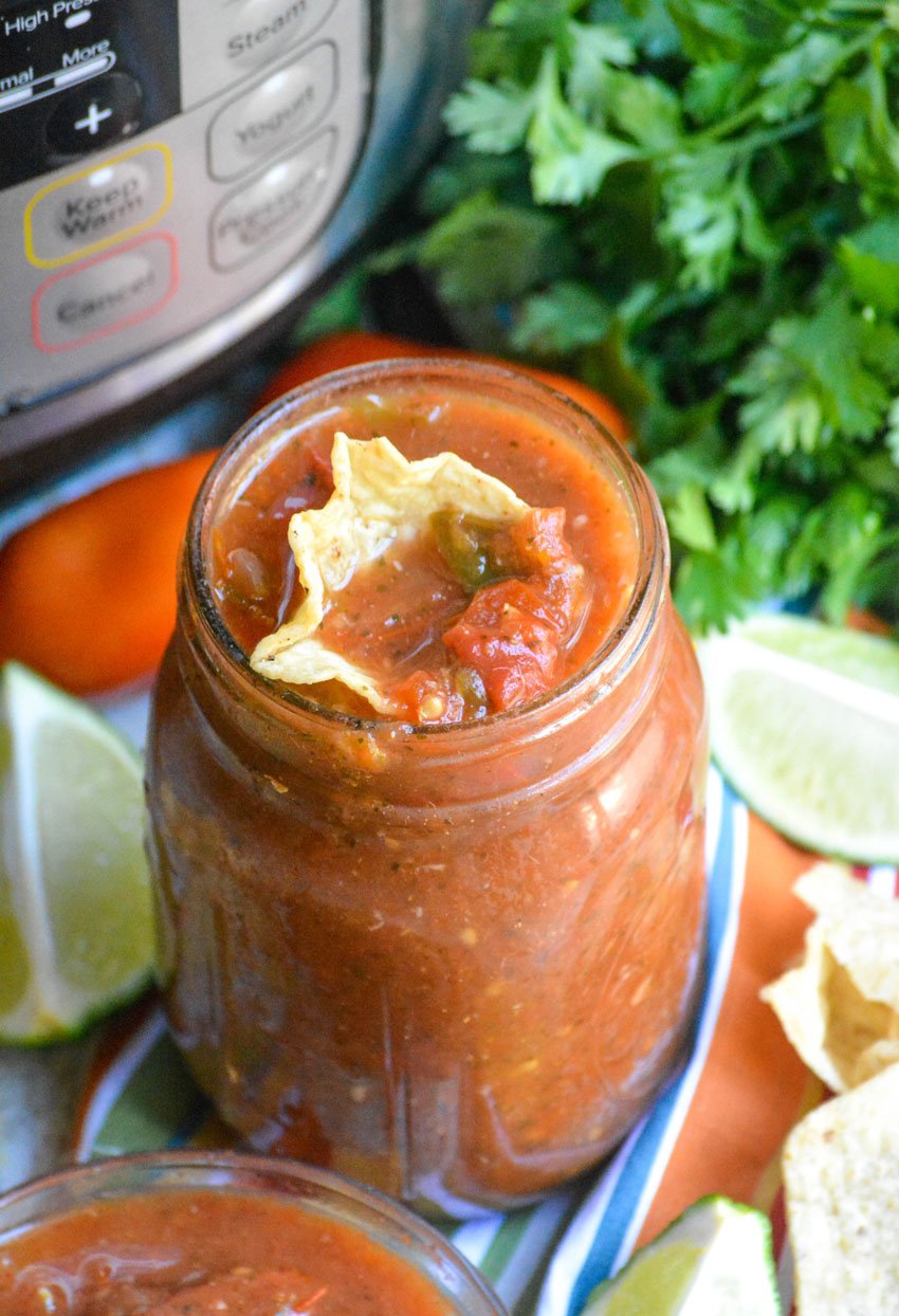 a scooped tortilla chip dipped in a mason jar filled with instant pot salsa