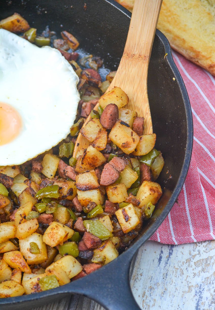 a wooden spoon in a skillet of hot dog hash with peppers and onions