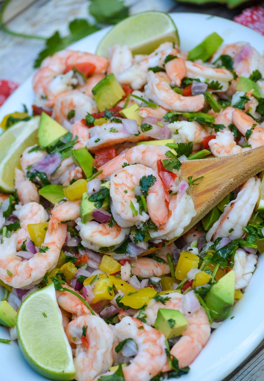 a wooden spoon digging into a bowl of shrimp ceviche with diced avocado