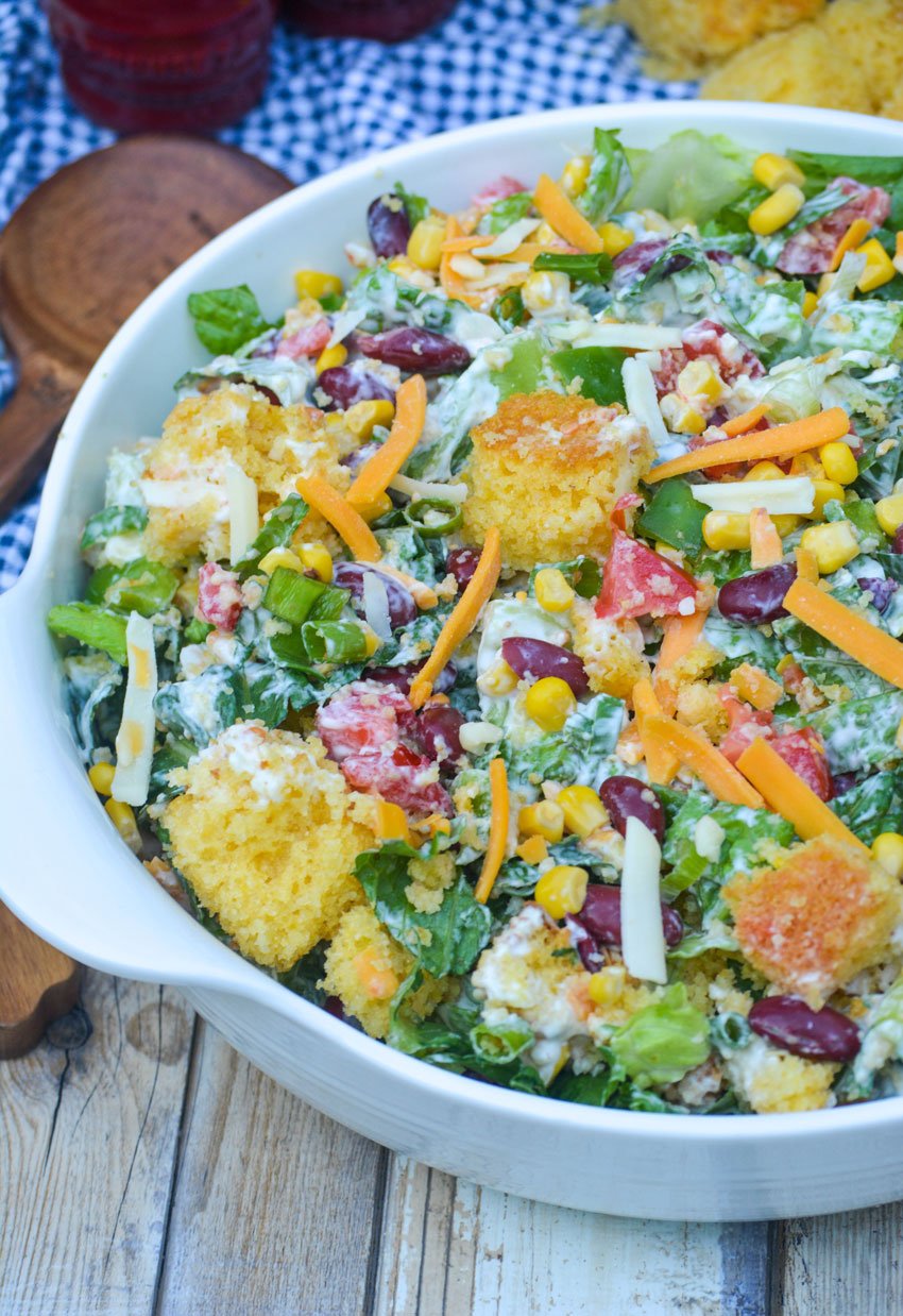 sweet corn bread salad topped with shredded cheese in a white serving bowl