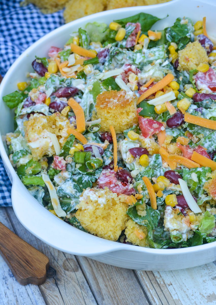 Southern cornbread salad topped with shredded cheese in a white serving bowl