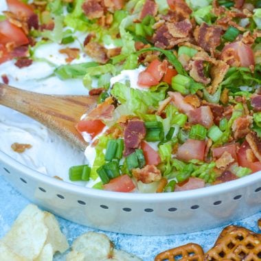a wooden spoon digging into a shallow dish filled with blt dip