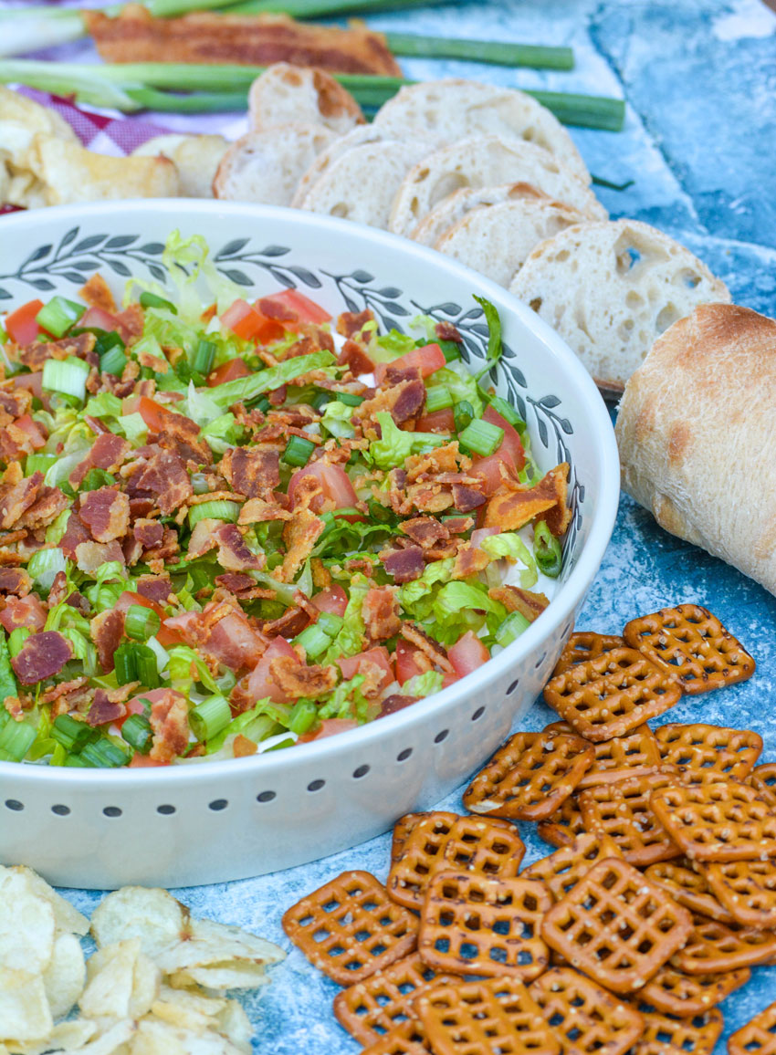 creamy blt dip in a shallow serving bowl topped with shredded lettuce, crumbled bacon, diced tomatoes, and thinly sliced green onions