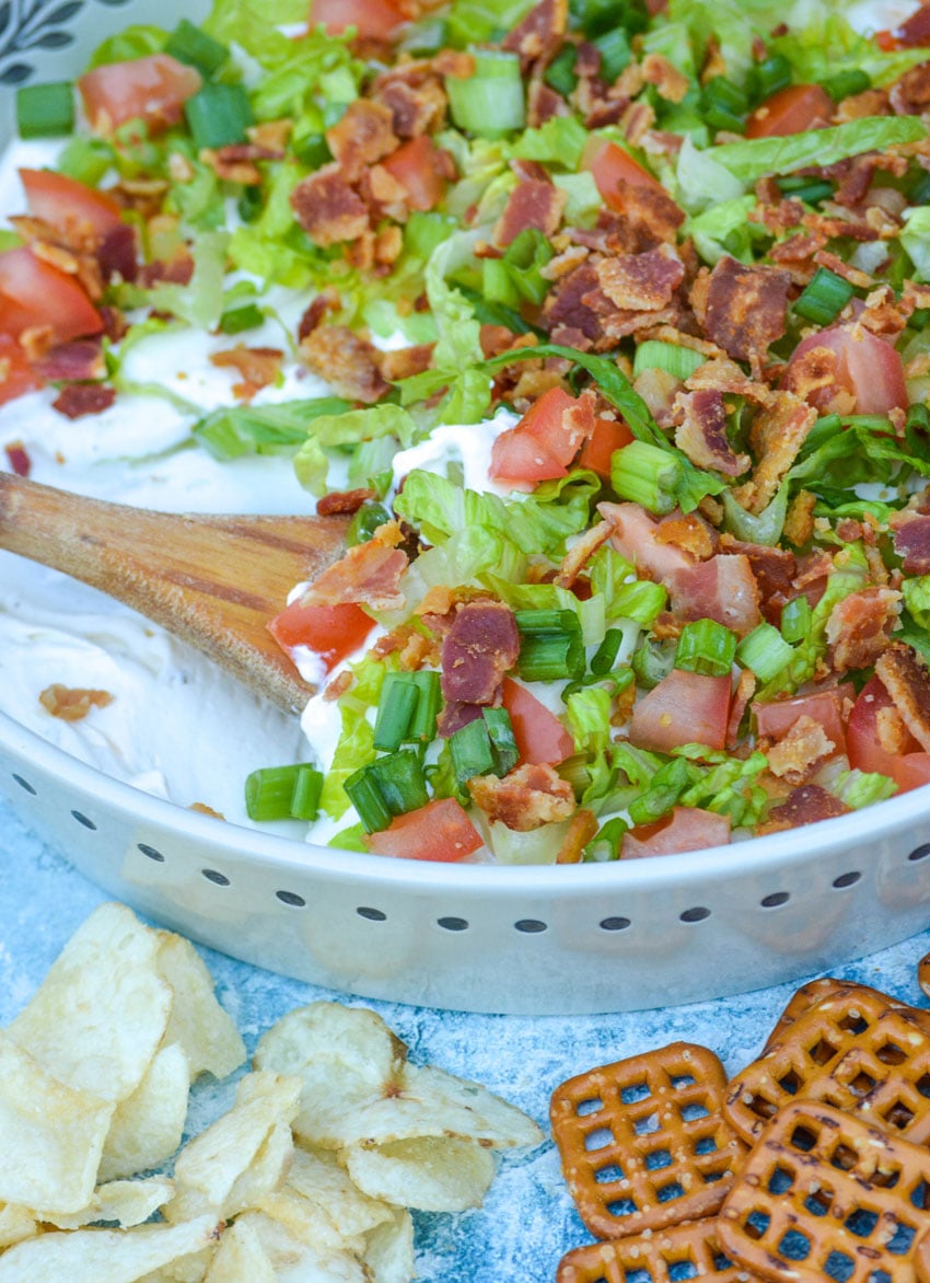 a wooden spoon digging into a shallow dish filled with blt dip