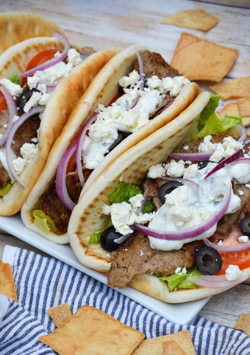 homemade gyros arranged in a row on a white platter