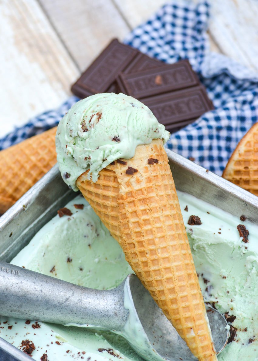 a scoop of no churn mint chocolate chip ice cream in a sugar cone resting on the edge of a metal loaf pan