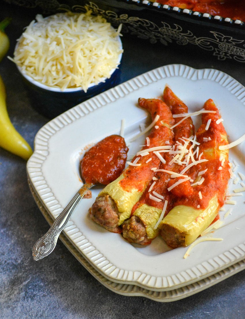 sausage stuffed banana peppers on a white plate with a silver spoon of marinara sauce on the side