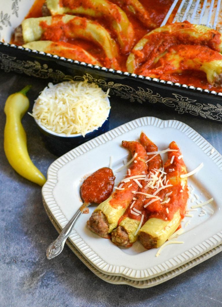 sausage stuffed banana peppers on a white plate with a silver spoon of marinara sauce on the side