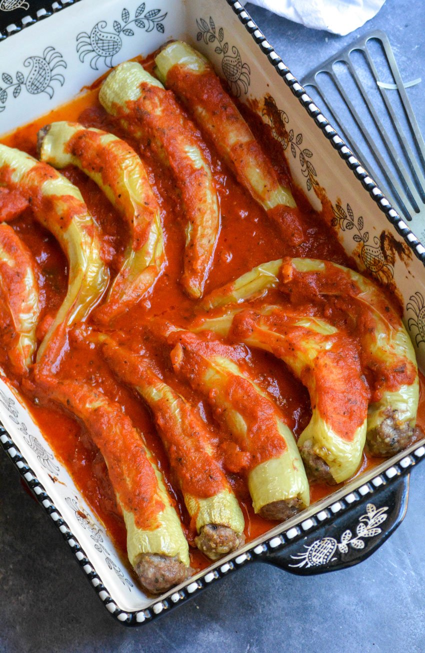 sausage stuffed banana peppers covered in red sauce in a black and white casserole dish