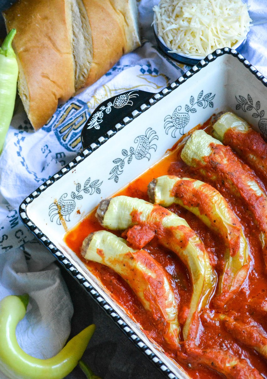 sausage stuffed banana peppers covered in red sauce in a black and white casserole dish