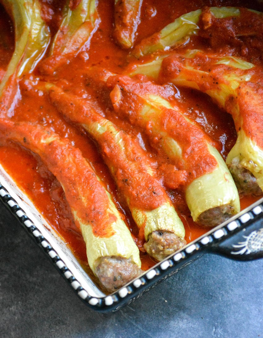 Italian style stuffed banana peppers covered in marinara sauce in a black and white casserole dish