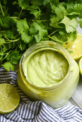smoked cilantro lime cream sauce in a glass jar surrounded by fresh cilantro leaves and sliced limes