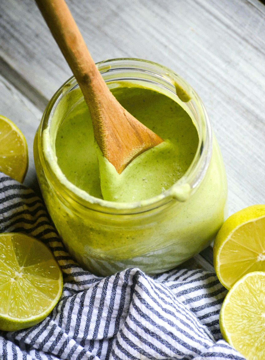 a wooden spoon stuck in a jar of green cilantro lime crema sauce