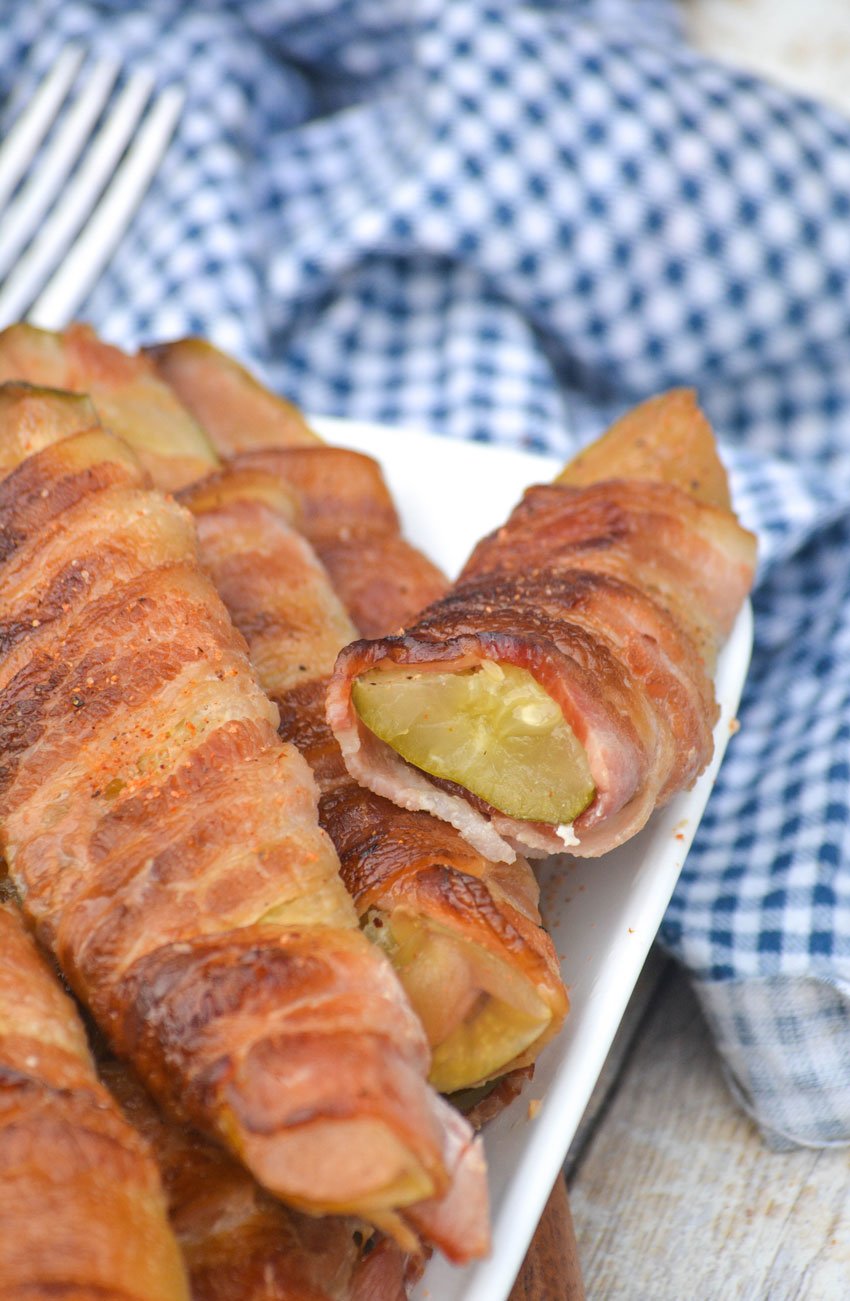 a stacked pile of bacon wrapped smoked pickle fries on a white serving platter