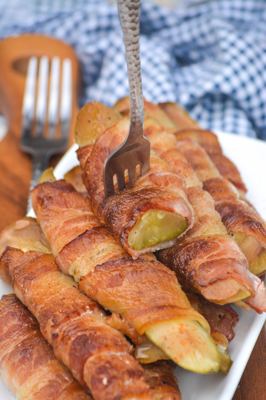 a silver fork stuck in a pile of crispy smoked pickles wrapped in bacon