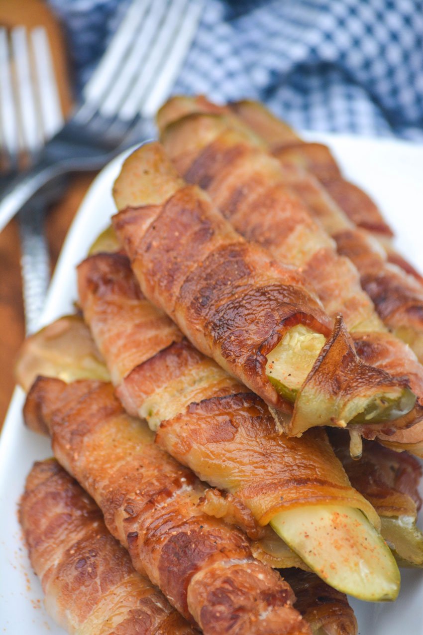 a stacked pile of bacon wrapped smoked pickle fries on a white serving platter