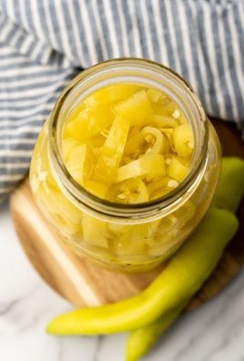 pickled banana pepper rings in a glass jar sitting on a wooden cutting board