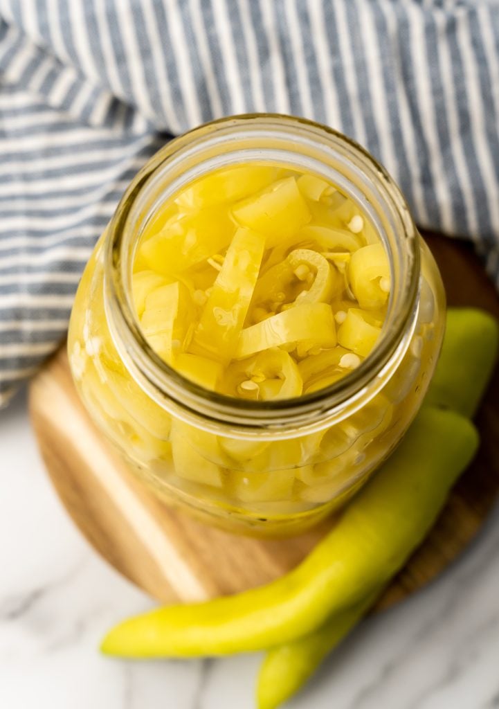 pickled banana pepper rings in a glass jar sitting on a wooden cutting board
