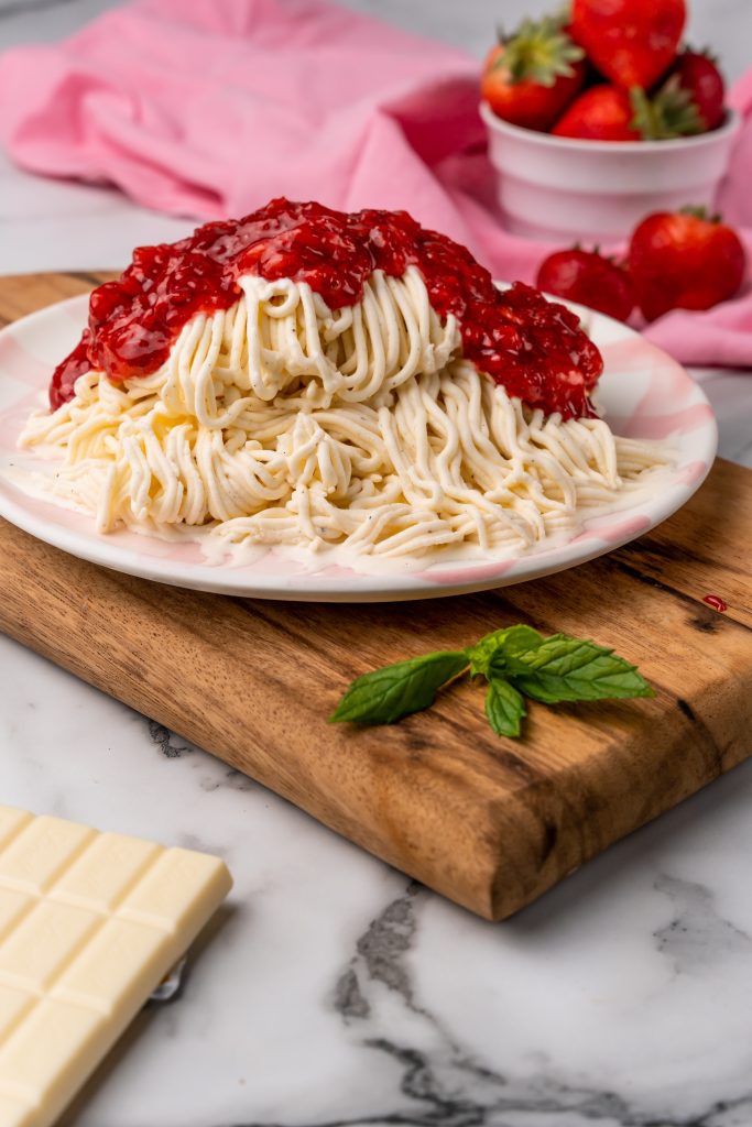 strawberry sauce topped ice cream noodles on a large dinner plate