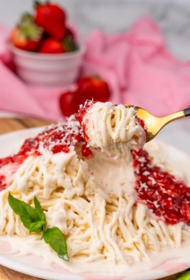a gold spoon holding up a scoop of strawberry topped spaghetti eis ice cream noodles