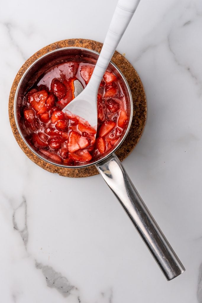 homemade strawberry sauce in a metal pot with a white spoon