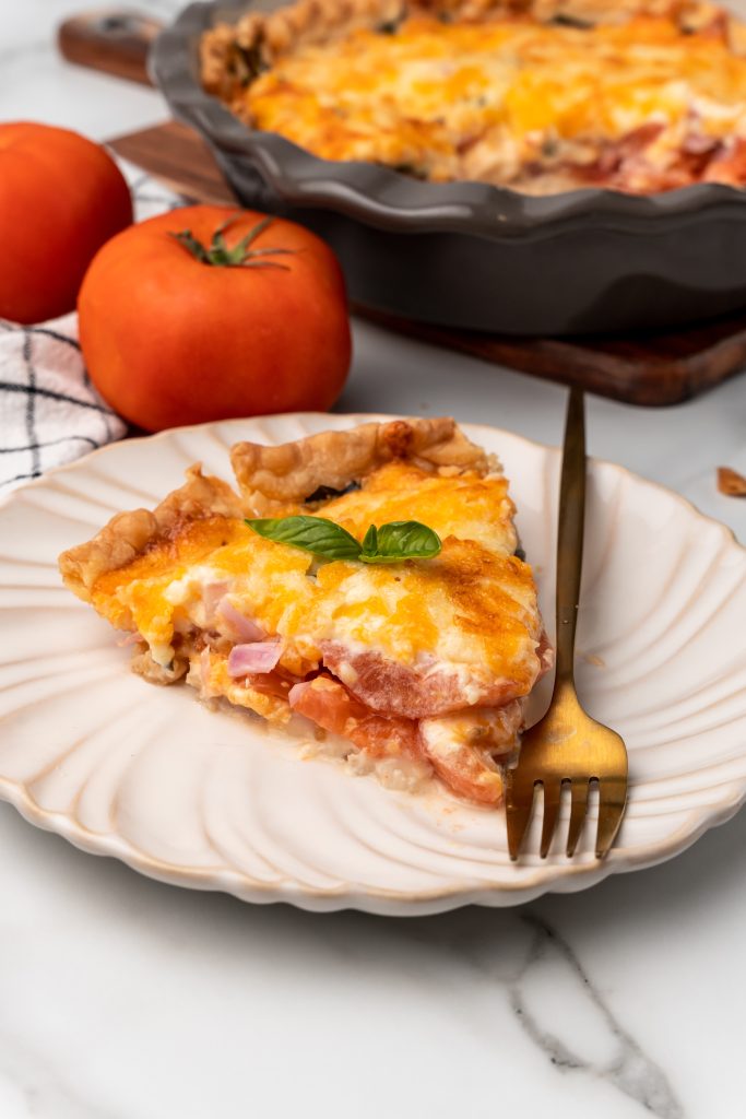 a slice of cheesy tomato pie on a white plate with a gold fork on the side