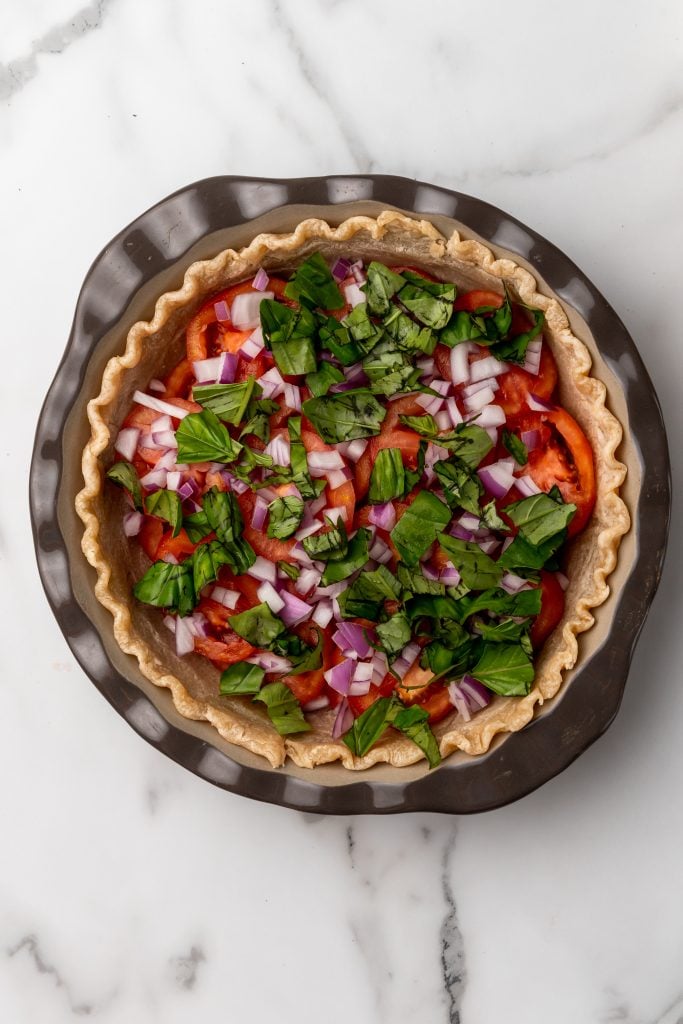 basil, onions, and tomatoes layered in a deep dish pie crust