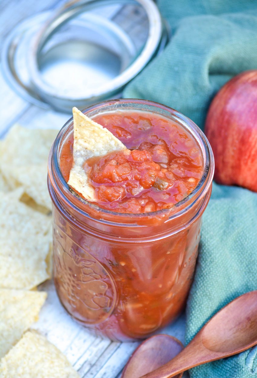 a tortilla chip dipped in a glass mason jar filled with apple salsa