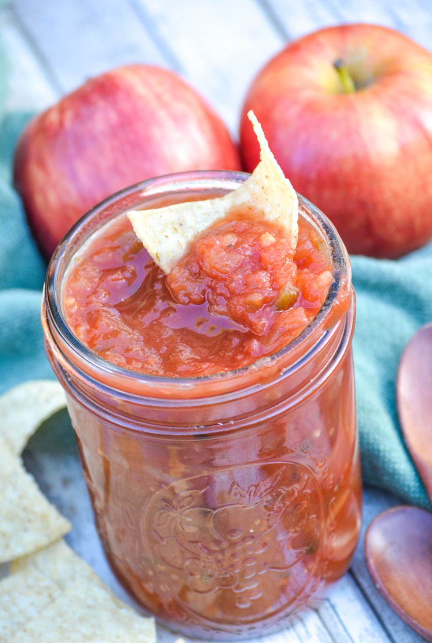 a tortilla chip dipped in a glass mason jar filled with apple salsa
