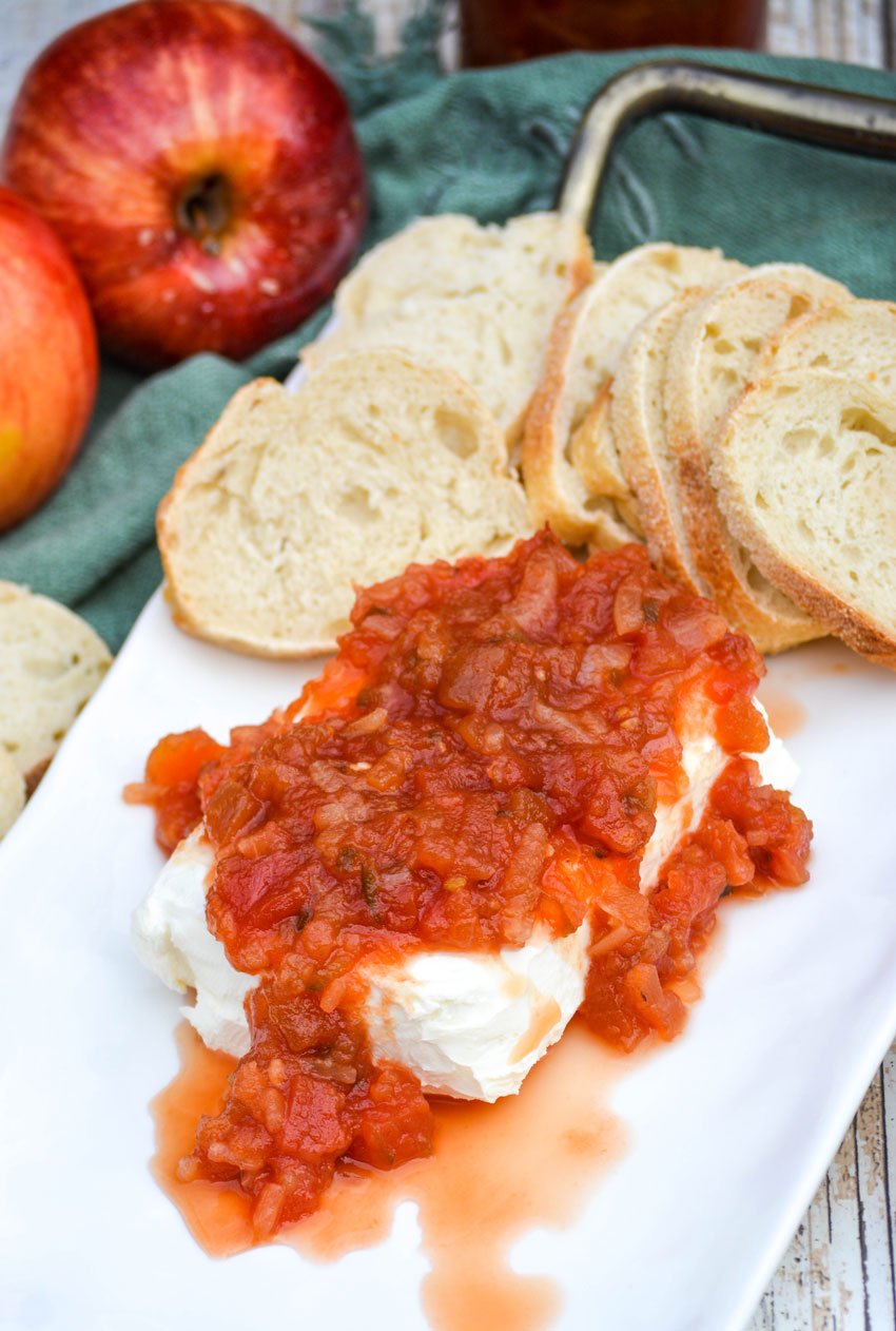apple salsa poured over a block of softened cream cheese served on a white platter with baguette slices