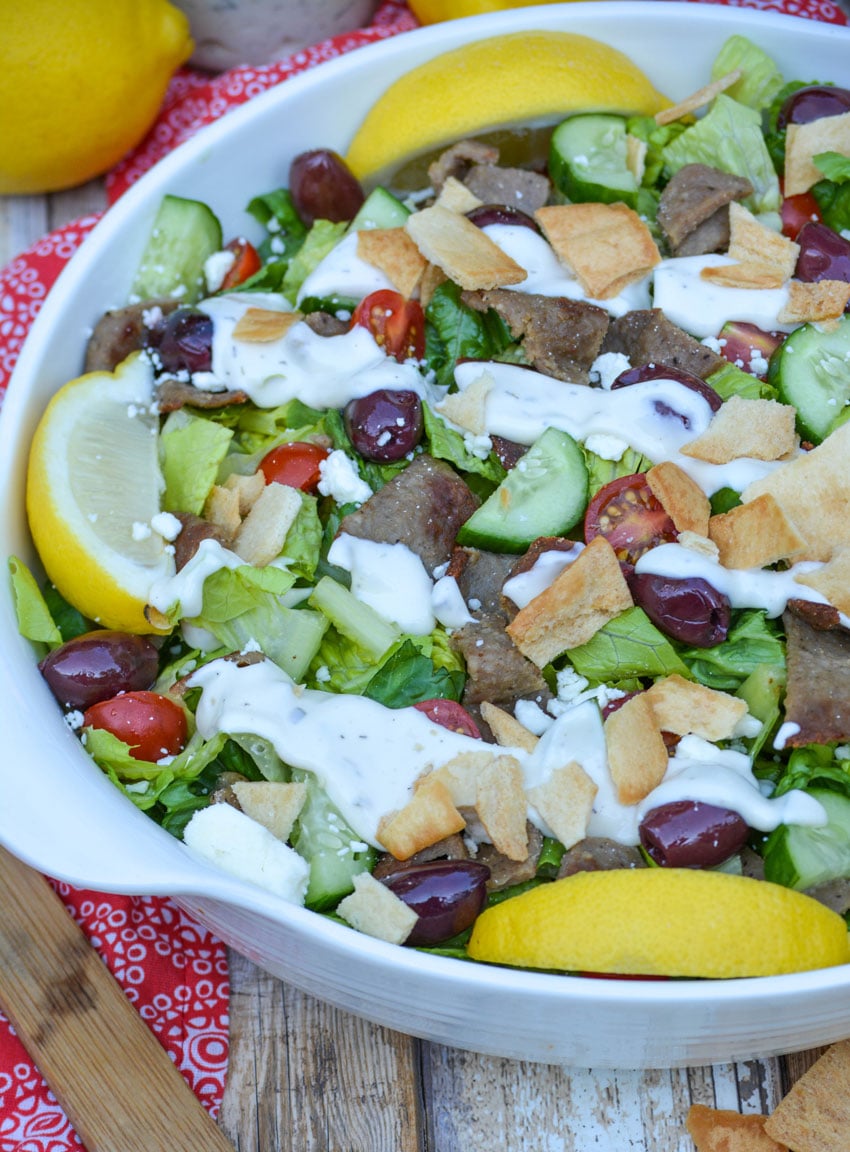 easy gyro salad in a white bowl with lemon wedges on the side