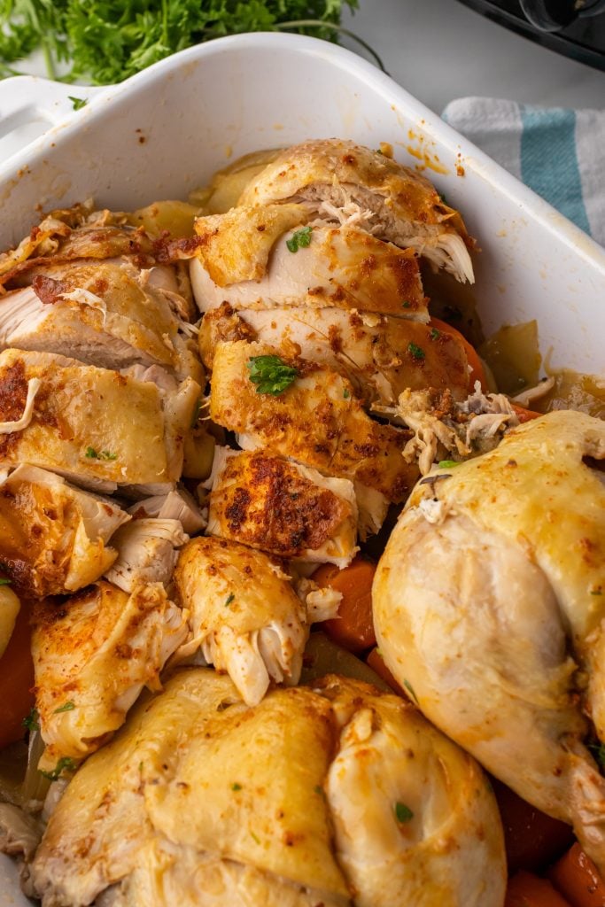 pieces of a cut up roasted crockpot chicken in a white casserole dish