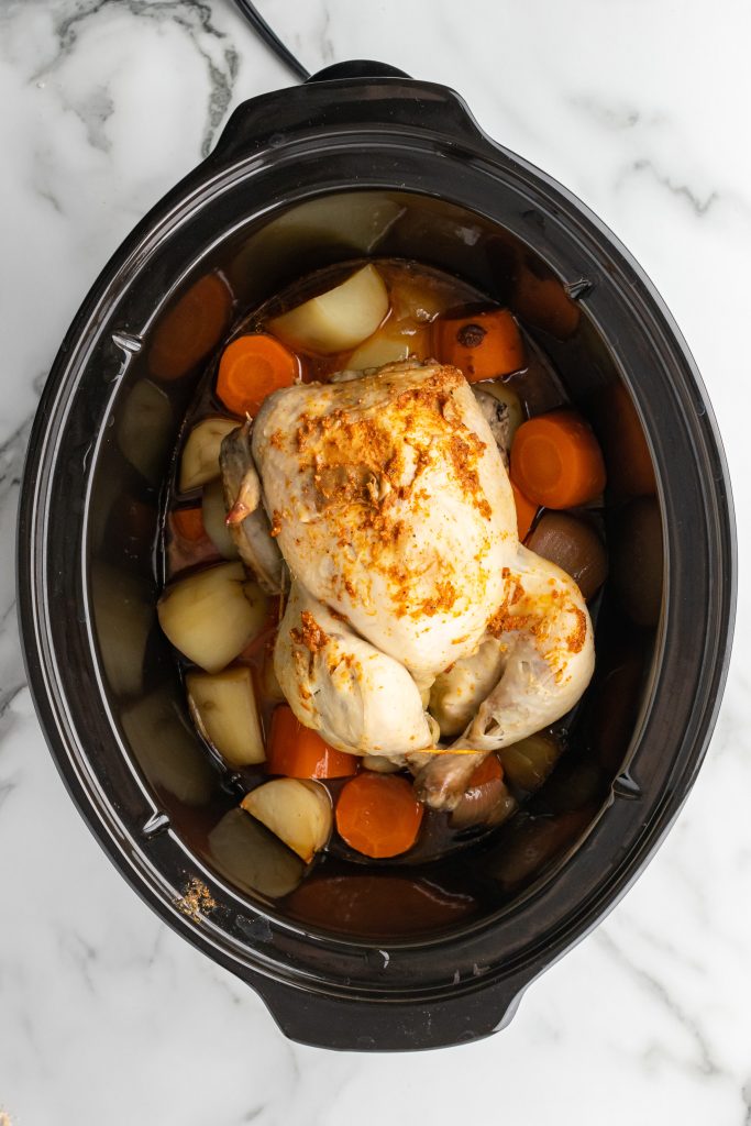 cooked slow cooker whole chicken in a black crock