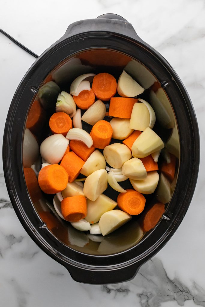 slices of onion carrots and potato in the bottom of a black crockpot