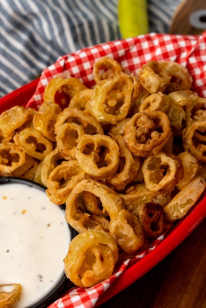 deep fried banana peppers in a red basket lined with checkered paper with a bowl of ranch for dipping