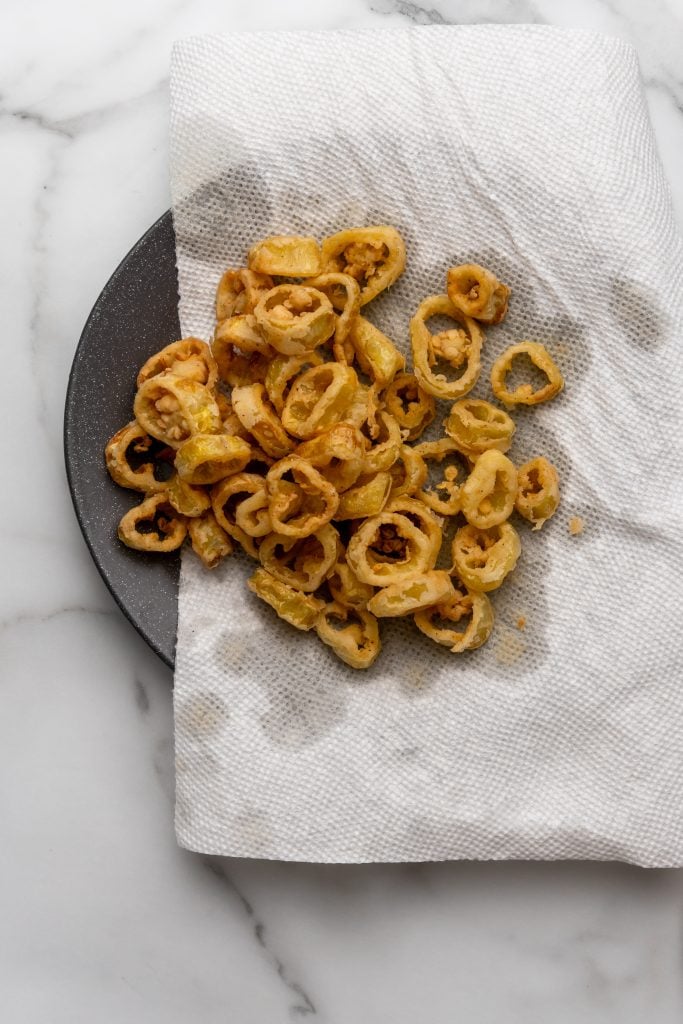 fried banana peppers draining on a paper towel lined plate