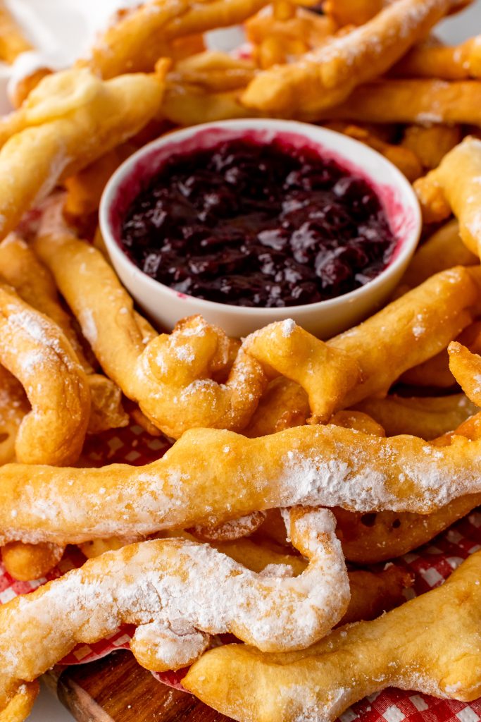 powdered sugar sprinkled funnel cake fries in a tissue paper lined basket